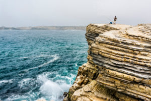Europe, Portugal, Centro Region, Peniche, lone angler on a ledge by the sea Europe, Portugal, Centro Region, Peniche, lone angler on a ledge by the sea